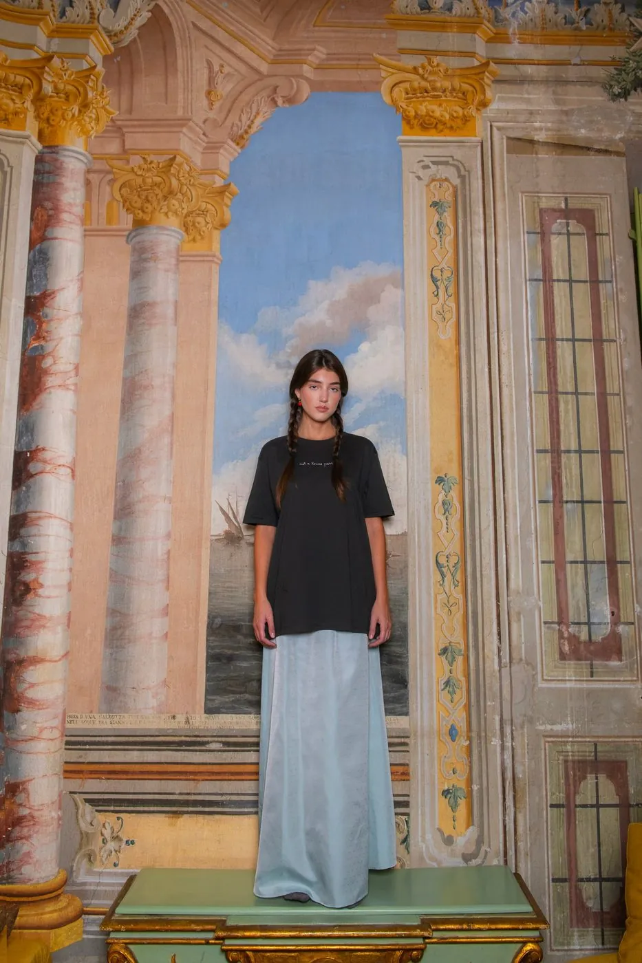 A model in front of frescoes with painted columns and a seascape