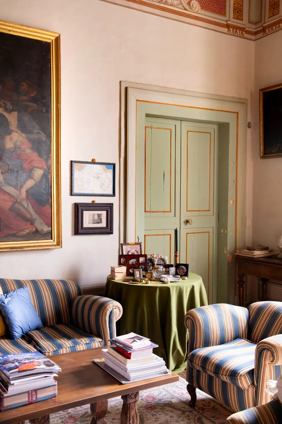The sitting room with striped sofas, a large painting in a gilded frame and a door painted green