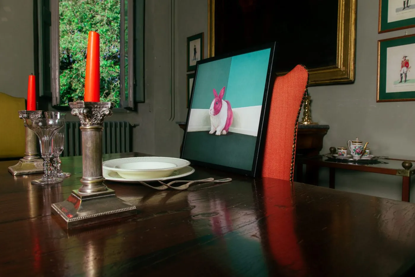 A print of a rabbit propped against a chair, on a table laid with candles